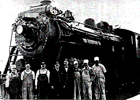 Working fashions for railway men posing in front of a steam locomotive.