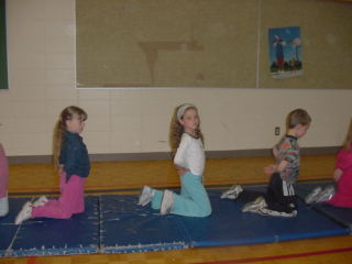 Grade 1 and Kindergarten girls swimming like seahorses on gym mat.